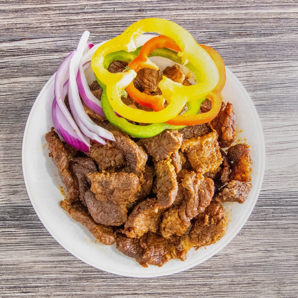 Plate of cooked meat pieces garnished with red onion slices and colorful bell peppers on a wooden table.