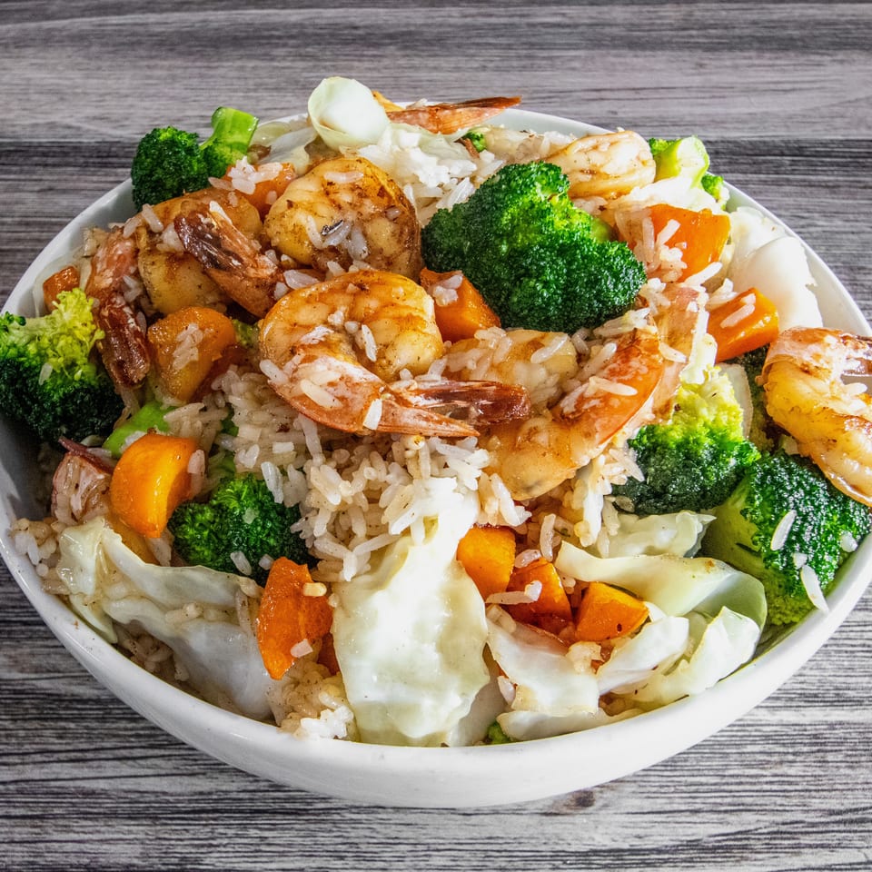 Shrimp and rice bowl with broccoli, carrots, and cabbage on a wooden table.