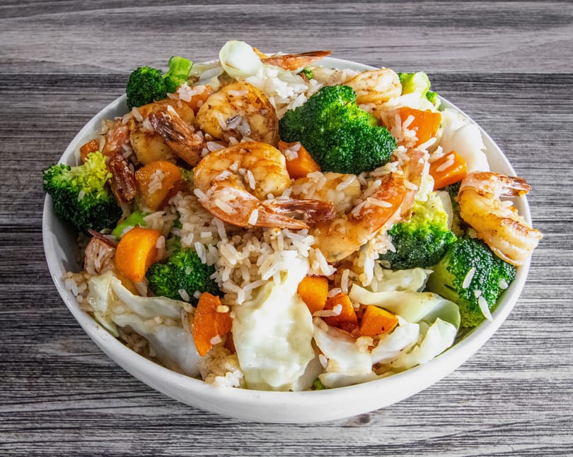 Shrimp and rice bowl with broccoli, carrots, and cabbage on a wooden table.