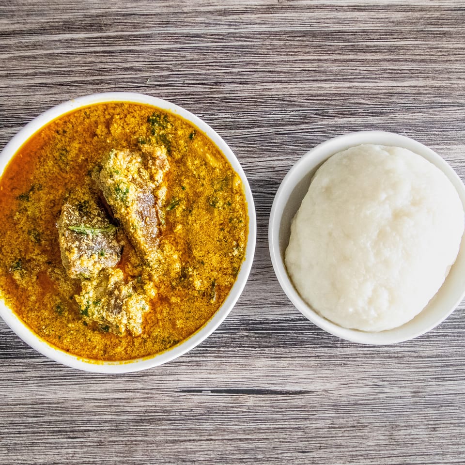 Overhead view of a bowl of Egusi soup with meat and a side of fufu on a wooden table.