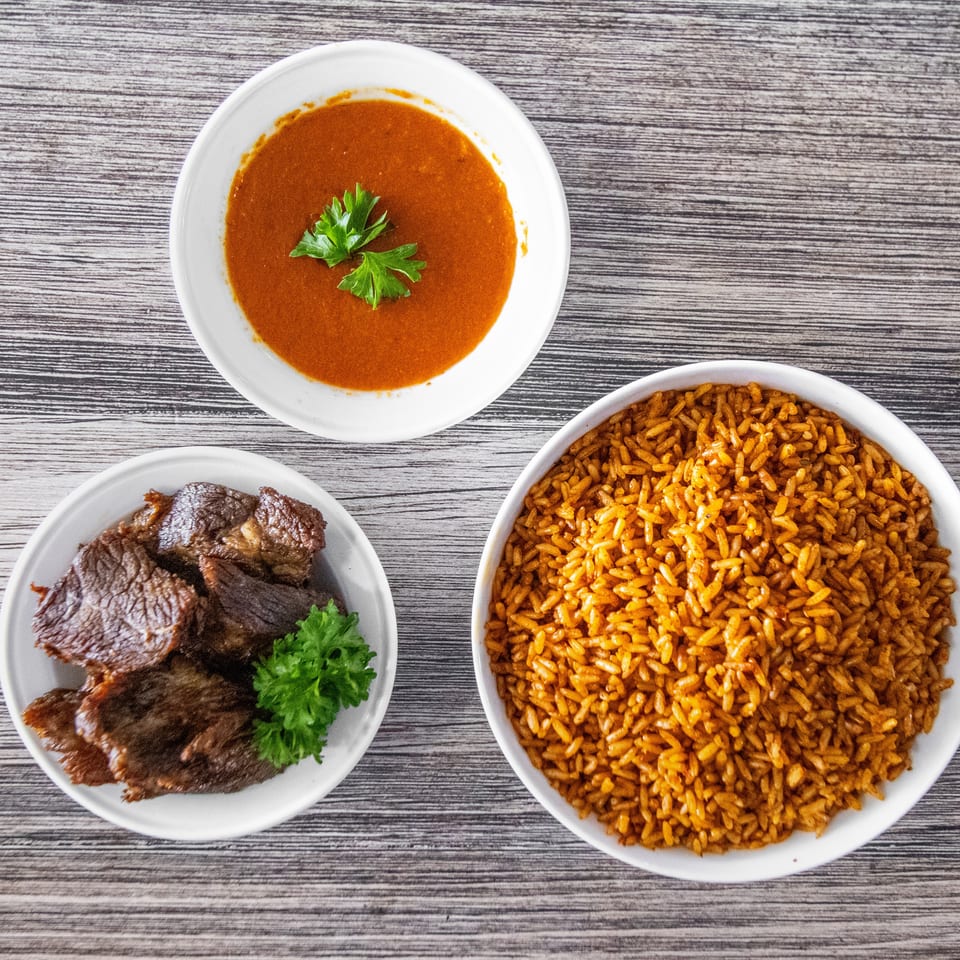 Three bowls of food: Jollof rice, stewed meat with parsley, and red soup on a wooden table.