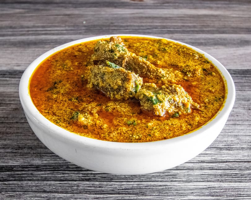 A white bowl filled with a vibrant orange curry and textured meat pieces on a wooden surface.