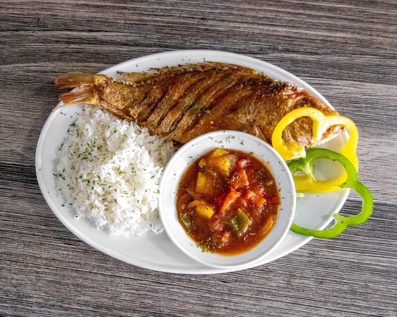 Crispy whole fried fish served with white rice, vegetable stew, and bell pepper slices.