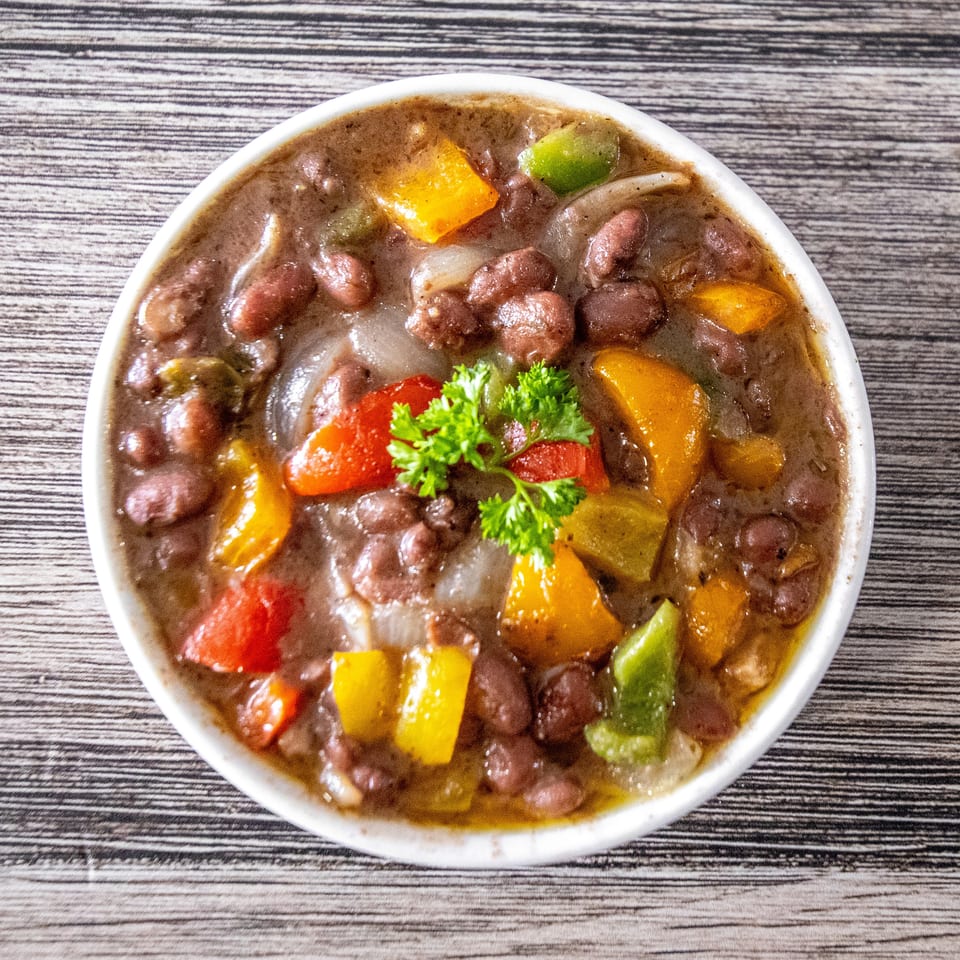 Bowl of red beans with colorful bell peppers, onions, and parsley on a wooden table.