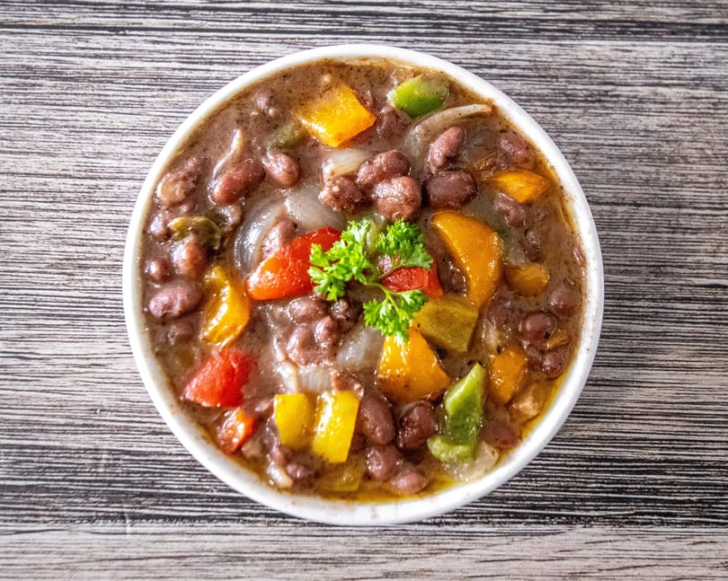 Bowl of red beans with colorful bell peppers, onions, and parsley on a wooden table.