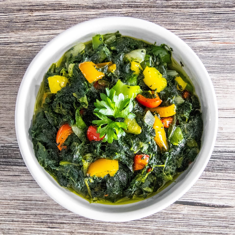 Overhead view of a vibrant green vegetable dish with colorful peppers and fresh parsley.