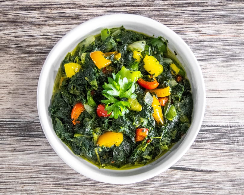 Overhead view of a vibrant green vegetable dish with colorful peppers and fresh parsley.