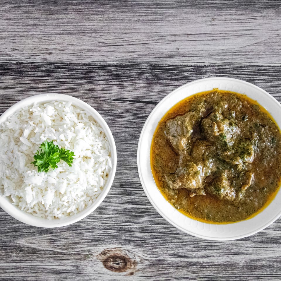 White rice with parsley and a bowl of green curry with meat on a wooden table.