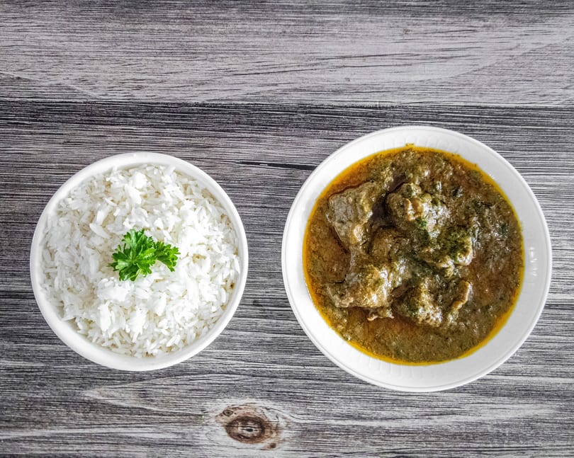 White rice with parsley and a bowl of green curry with meat on a wooden table.